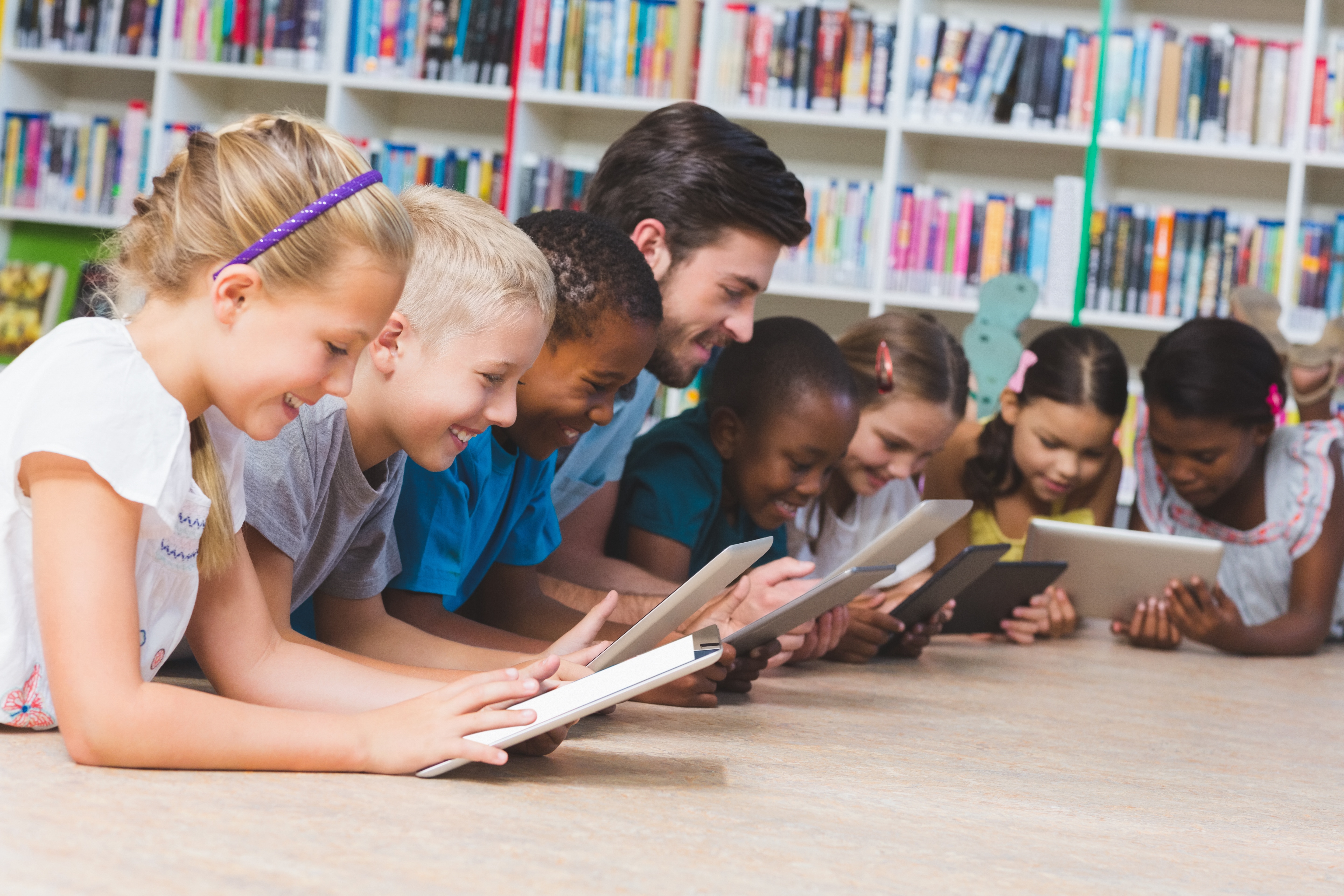Teacher and kids lying on floor using digital tablet in library tablets management at school